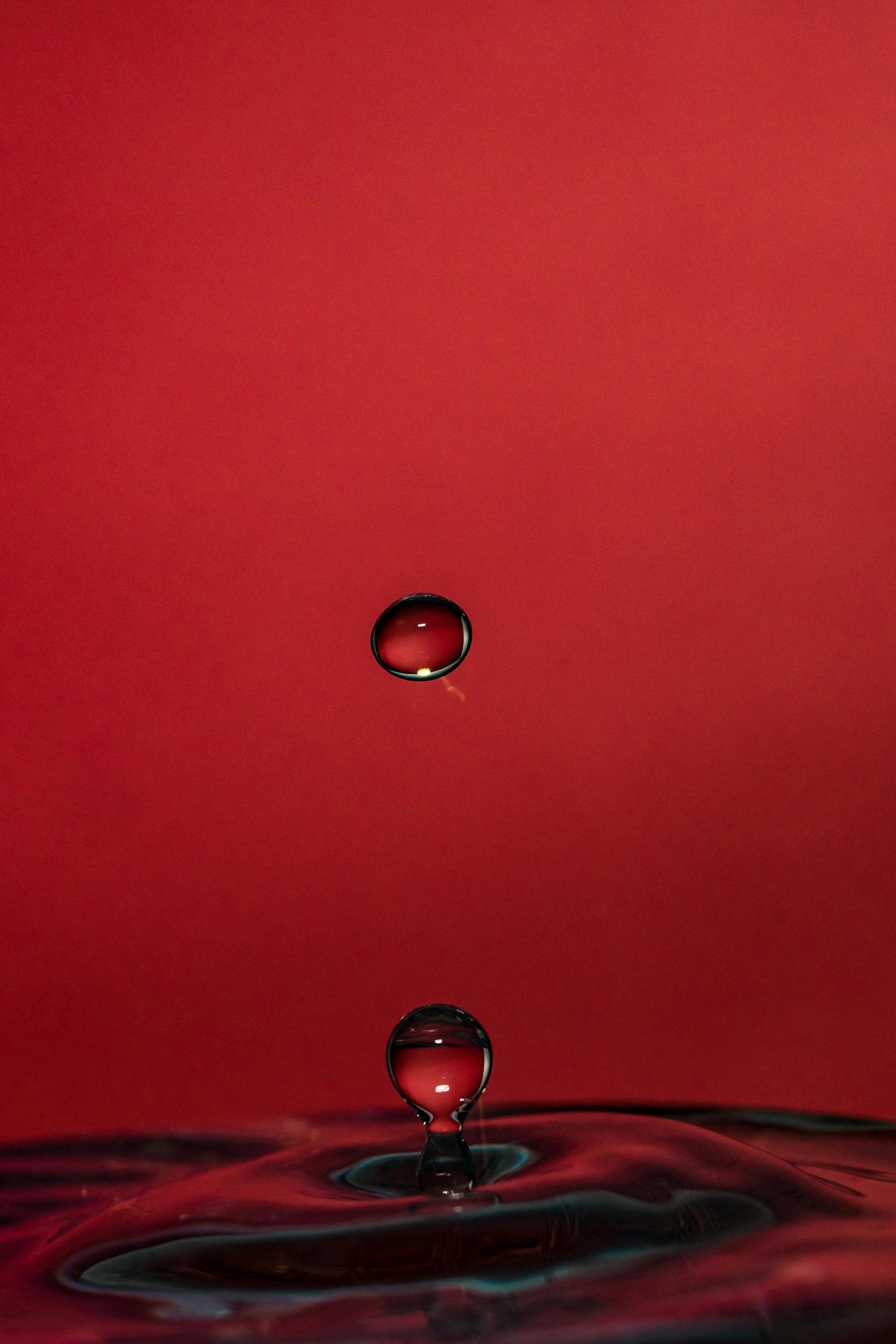 A captivating close-up of a water drop creating ripples on a red backdrop. Perfect for backgrounds.